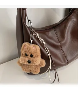 Plush brown dog bag charm with metal bone tag hanging on a leather handbag detail