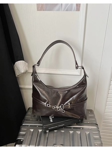 Detail of glossy coffee leather shoulder bag with silver chain buckle on a silver suitcase