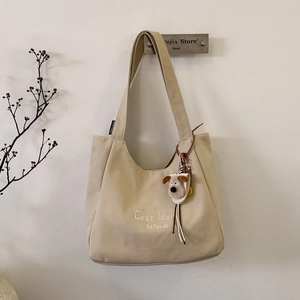 Detail of beige canvas shoulder bag with embroidery and plush puppy keychain charm
