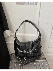 Detail of black glossy crescent hobo bag with silver buckle on a metallic suitcase