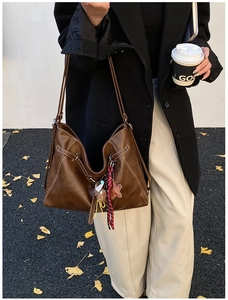 Detail of dark brown hobo bag with contrast stitching and decorative charms on strap