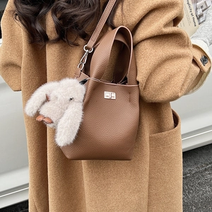 Detail of brown litchi pattern leather bucket bag with silver lock and plush rabbit charm