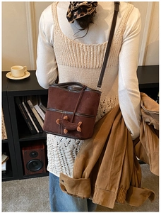 Brown suede bucket bag with white stitching and dog charm shown in a retro scene