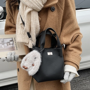Close-up of black litchi pattern bucket bag with silver lock and plush rabbit charm