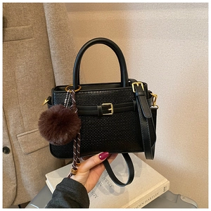 Detail shot of black embossed bucket bag with gold buckle and fuzzy charm accessory