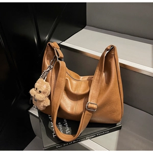 Detail of a brown leather shoulder bag with a silver buckle and cute plush bear charm