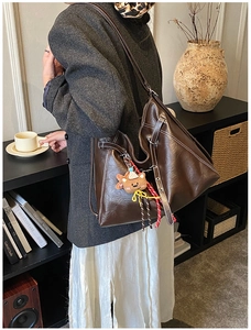 Detail of deep brown leather tote bag with white contrast stitching and bear pendant