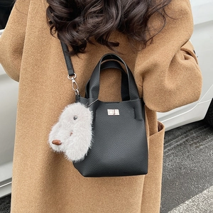 Detail of black pebbled leather bucket bag with metal lock and white plush pendant accessory