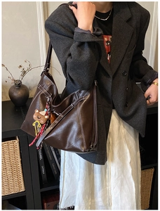 Detail of dark brown leather tote bag with white contrast stitching and bear charm