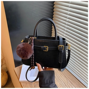 Detail of black woven crossbody bag with gold hardware and plush charm decoration