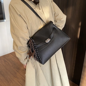 Detail of black litchi pattern tote bag with silver lock and brown pony charm on person