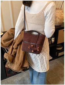 Detail of dark brown suede bucket bag featuring white contrast stitching and plush puppy charm