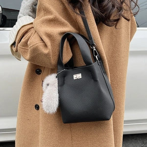 Close-up of black lychee grain leather bucket bag with metal lock and plush charm