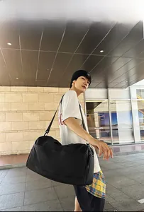 Black travel bag shown worn by model in urban setting with adjustable shoulder strap