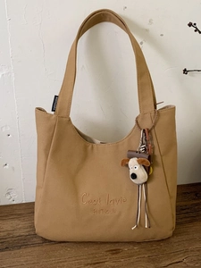 Khaki canvas tote bag with 'C'est lavie' embroidery and plush dog charm on wood surface