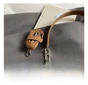 Close-up of brown leather shoulder bag with H-shaped silver buckle and white stitching