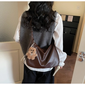 Detail of dark brown hobo bag with plush bear charm worn as a shoulder bag