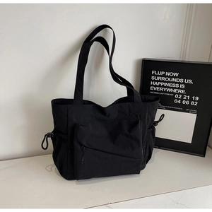 Detail of black nylon tote bag with front zipper pocket and side drawstring on marble table