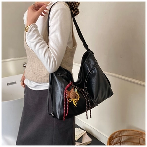 Side view of black faux leather hobo bag with contrast white stitching and bear charm