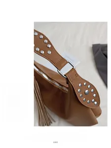 Detail of tan leather shoulder bag featuring silver metal rivets and long side tassels