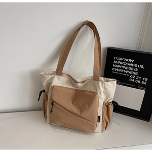 Detail of a color-block tote bag featuring side drawstring pockets and a front zipper pocket