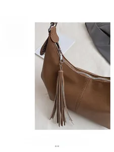 Macro detail of brown leather hobo bag featuring smooth silver zipper and long tassel charm