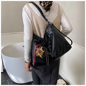 Detail of black tote bag with white contrast stitching, buckles and bear pendant