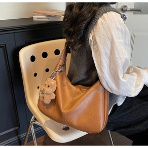 Close-up of caramel brown hobo bag featuring plush bear pendant and leather texture