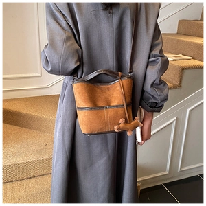 Detailed shot of brown suede bucket bag with leather trim and horse charm on a model