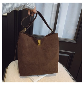 Detail of dark brown suede bucket bag with vintage gold clasp on a soft white chair