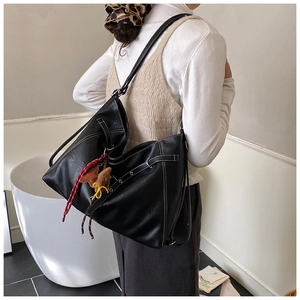 Detail of black leather hobo bag with contrast white stitching and decorative charms