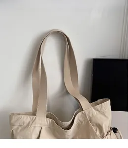 Close-up of the beige canvas tote bag showing wide shoulder strap and side pleat detail