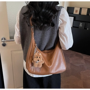 Brown hobo shoulder bag with a cute plush bear pendant shown on model in home setting