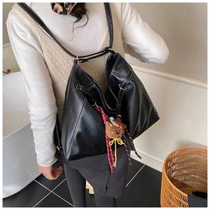 Detail of black glossy PU leather tote bag with white stitching and teddy bear charm