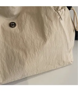 Close-up of cream nylon tote bag with pleated texture and round CM metal logo detail