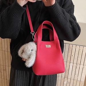 Detail of red bucket bag with leather texture, turn-lock closure and plush bunny charm