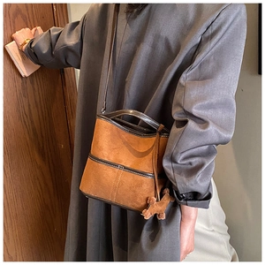Detail of vintage brown suede bucket bag with leather trim and plush puppy charm accessory