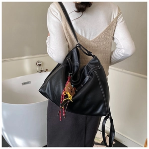 Detail of black tote bag with white stitching and bear charm on a model's shoulder