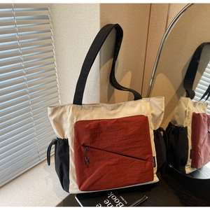 Detail of multi-color tote bag featuring red zipper pocket and beige nylon texture