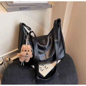 Detail of black hobo bag with vertical stitching and brown teddy bear charm