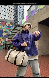 Large beige travel duffel bag with black straps being carried by a model on a city street