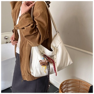 Detail of white PU leather shoulder bag featuring a cute brown bear charm and braided ropes