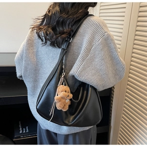 Macro shot of black PU leather hobo bag with cute brown plush bear pendant detail