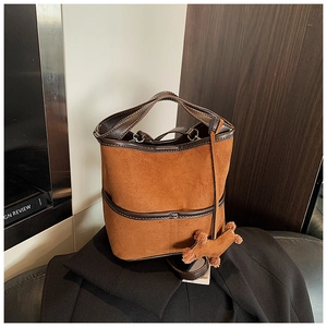 Detail of caramel suede bucket bag with leather trim and cute puppy plush charm