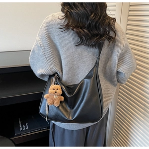 Close-up of a matte black hobo bag with a plush bear charm worn by a model in grey sweater