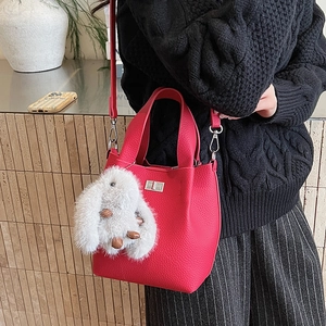 Detail of red pebbled leather bucket bag with metal twist lock and white rabbit fur charm