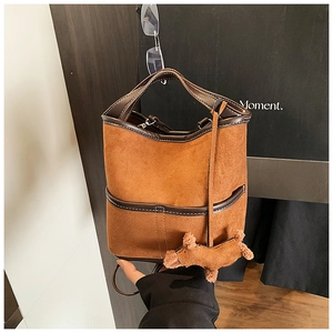 Close-up of brown suede bucket bag featuring leather trim and a cute puppy plush charm