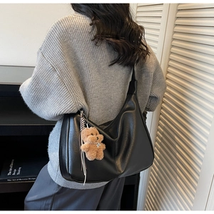 Detail of black leather hobo bag with texture, wide strap and brown teddy charm
