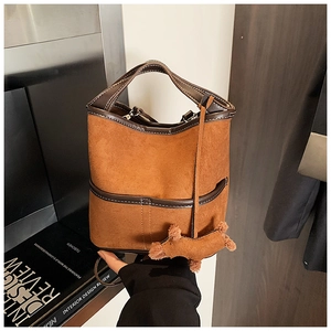Detail of a brown suede bucket bag with leather piping and a cute plush dog charm accessory