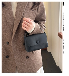 Close-up of elegant black leather handbag with round buckle and single top handle detail